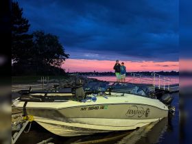 Two friends pose on the dock beside their boat at sunset, capturing a memorable moment against a stunning twilight backdrop.
