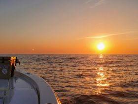 A serene sunset view from the bow of a boat, casting golden reflections on the ocean's surface — perfect for tranquil evening cruises.