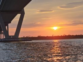 A stunning sunset view framed by a bridge, reflecting beautifully on the water — a picturesque moment perfect for evening boat trips.