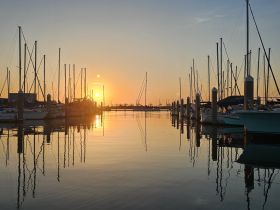 A stunning sunset over a marina, with boats silhouetted against the vibrant sky, creating a picturesque scene perfect for evening strolls or romantic outings.