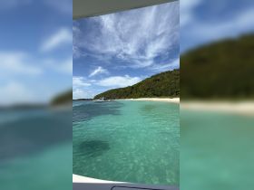 A stunning view of a tranquil beach with crystal-clear waters and lush greenery, perfect for a relaxing day on the water.