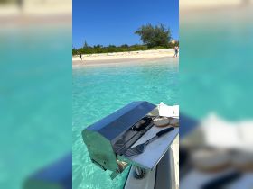 A grill setup on a boat with cooking utensils and buns, perfect for a beach barbecue experience. Guests can be seen enjoying the sandy shoreline in the background.