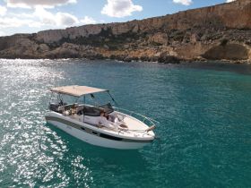 A couple relaxes on the deck of a boat, surrounded by stunning turquoise waters and rocky cliffs — an idyllic setting for a romantic getaway.