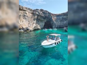 A group enjoys a day on the water near a stunning cave, with one person standing on the boat, showcasing the vibrant turquoise waters — perfect for adventure seekers and scenic tours.