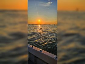 A serene sunset view over calm waters, captured from the edge of a boat, creating a picturesque backdrop for evening cruises.