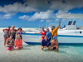 A lively group poses for a photo at a sandbar stop, enjoying their time by the boat 'Catalyst' — a perfect backdrop for memorable adventures on the water.