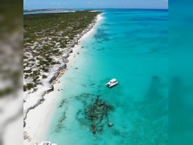 A stunning aerial view of a boat cruising through crystal-clear turquoise waters, showcasing the beautiful coastline and sandy beaches — perfect for exploring the serene landscapes of the Bahamas.