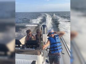 A joyful group enjoys a boat ride, with a child playfully posing at the helm, showcasing the fun of family outings on the water.