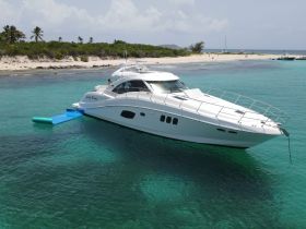 A stunning aerial view of the 'Lucky Penny' yacht docked in crystal-clear waters, showcasing its sleek design against a picturesque beach backdrop.