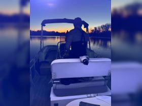 A serene sunset view from a boat with a person at the helm, capturing the tranquil beauty of evening on the water.