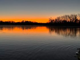A stunning sunset casts vibrant colors over the water, creating a serene reflection — perfect for capturing the beauty of nature during a peaceful evening on the water.