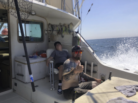 A relaxing moment on a fishing boat with a family, showcasing a father giving a thumbs up while his child rests nearby — perfect for family fishing trips on the ocean.