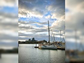 A serene view of a yacht docked at a marina, surrounded by a picturesque skyline and dramatic clouds, perfect for showcasing boating adventures.