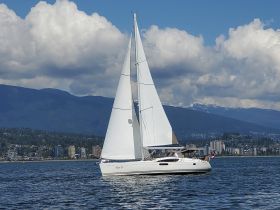 A beautiful sailboat glides through the water with majestic mountains in the background, showcasing the perfect day for sailing.