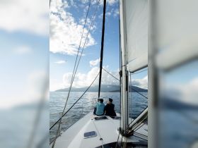 A couple enjoys a serene sailing experience, taking in breathtaking views of the ocean and mountains — perfect for romantic getaways or adventure-filled trips.