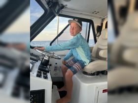 A young boy sits at the helm of a boat, showcasing the interior cabin space and steering controls — perfect for aspiring young captains.