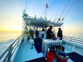 Fishermen prepare their gear aboard a boat as the sun sets over the tranquil waters, creating a perfect backdrop for a memorable fishing trip.