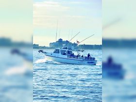 A fishing boat named 'FISH BOUND II' navigates the ocean waters, showcasing a lively day on the water with passengers enjoying the experience.