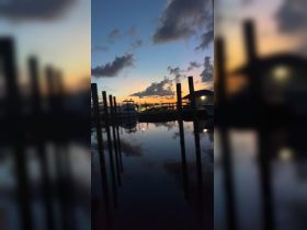 A blurry image of a marina at dusk, featuring boats and reflections in the water, creating a serene atmosphere.