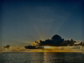 A scenic view of the sky at sunset, with clouds and rays of light reflecting over the water, creating a tranquil atmosphere.