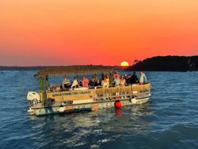 A lively group enjoys a sunset cruise aboard a tiki boat, creating unforgettable memories against a stunning backdrop of vibrant colors.