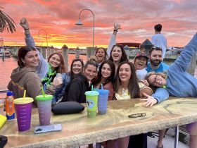 A lively group celebrates at sunset, enjoying drinks and good company by the water — perfect for memorable gatherings and parties.