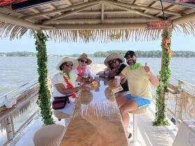 A lively group enjoys drinks at a tiki bar on a boat, celebrating with smiles and tropical vibes — perfect for a fun day on the water.