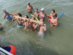 A lively group enjoys a fun day in the water, engaging in playful activities with drinks in hand — perfect for summer parties and celebrations.