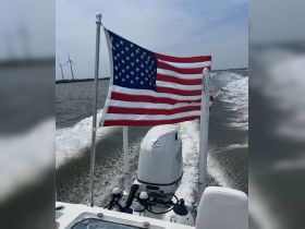 A striking view of a boat in motion, showcasing the American flag waving proudly against a backdrop of wind turbines — a perfect representation of nautical adventure.