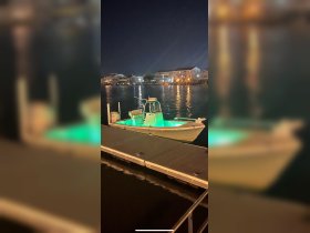 A beautifully illuminated speedboat docked at night, showcasing its sleek design against the tranquil waters and surrounding buildings.