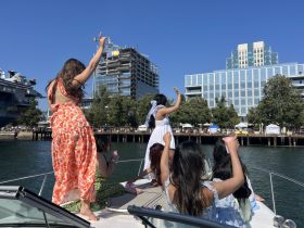 A lively group of friends celebrates on a boat, enjoying drinks and the sunny atmosphere — perfect for a fun day out on the water.
