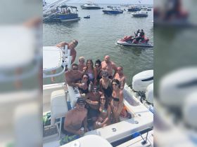 A lively group enjoys a fun day on the water, celebrating with drinks aboard a boat, surrounded by friends and other vessels in the background.