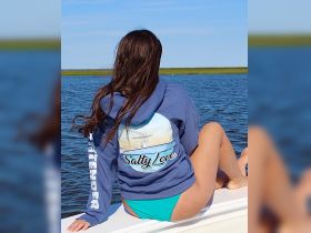 A young woman enjoys a serene moment on a boat, showcasing the beautiful water and her stylish 'Salty Love' hoodie — perfect for a day out on the water.