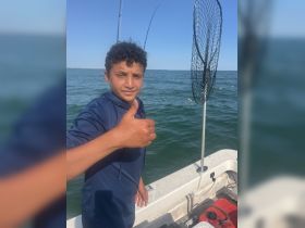 A young boy gives a thumbs up while fishing on a boat, capturing the joy of a day on the water. Perfect for family fishing adventures.