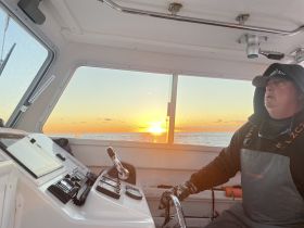 A captain navigates the boat at sunset, showcasing the serene beauty of the ocean — perfect for fishing trips or evening cruises.