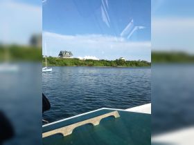 A scenic view from a boat showcasing a picturesque coastline with a charming house and a sailboat in the foreground, perfect for capturing the beauty of a day on the water.