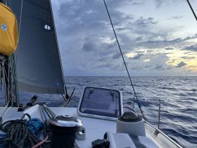 A close-up view of a sailboat's deck with sails raised, navigating through open waters under a dramatic sky, perfect for sailing enthusiasts.