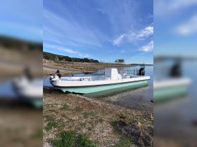 A sleek boat is docked on the shore, showcasing its design against a backdrop of clear skies and calm waters, perfect for fishing or leisure activities.