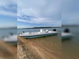 A sleek speedboat rests on a sandy shore, showcasing its streamlined design against a picturesque backdrop of water and hills.