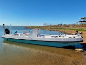 A sleek speedboat docked at the shore, showcasing its clean lines and modern design against a clear blue sky.