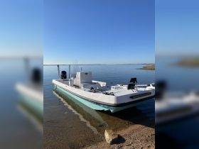 A sleek speedboat docked at the water's edge, showcasing its clean lines and modern design against a clear blue sky.