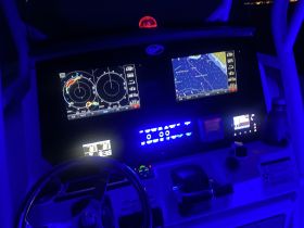 A close-up view of a boat's helm and navigation console, illuminated in blue light, showcasing advanced navigation equipment and controls.