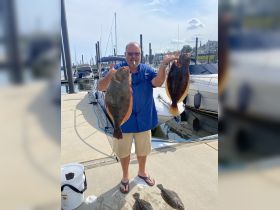 A proud angler displays his impressive catch of flounder at the marina, showcasing a successful day of fishing.