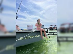 A young girl enjoys a refreshing pineapple drink while sitting on the edge of a Blazer Bay boat, capturing the essence of summer fun on the water.