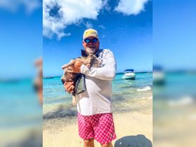 A man holds a pig while standing on the beach, showcasing a unique human-animal interaction in a picturesque tropical setting.