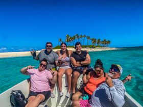 A joyful group poses on a boat near a picturesque beach, showcasing their fun-filled day in the sun — perfect for snorkeling and beach adventures.