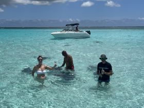 A lively group enjoys a sandbar stop, swimming in crystal-clear waters while sipping cocktails — the perfect setting for a fun day on the water.