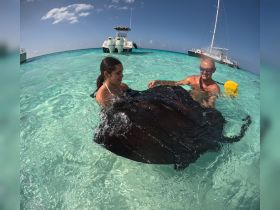 Two individuals interact with a stingray in shallow turquoise waters, showcasing a unique wildlife experience in a tropical setting.