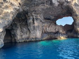 A stunning view of a natural rock formation with a cave opening, surrounded by vibrant blue waters — a picturesque destination for boat tours and exploration.