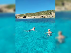 Two individuals enjoy a refreshing swim in crystal-clear waters, surrounded by stunning coastal scenery — a perfect highlight of a beach day.